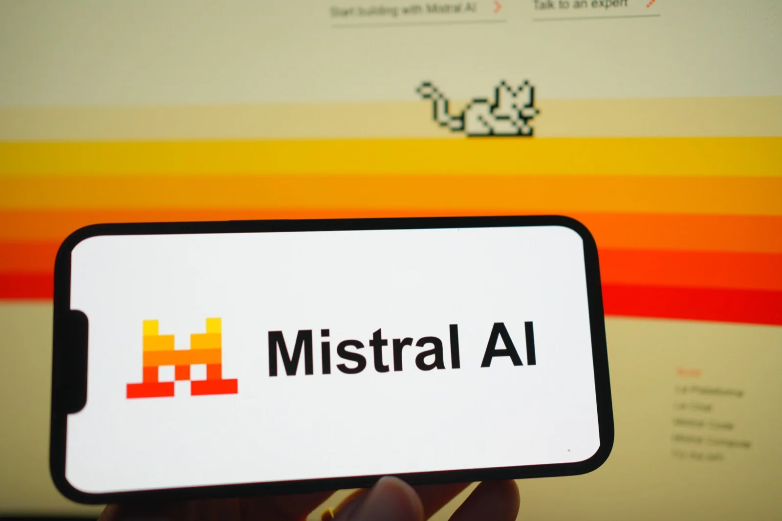 Phone screen displaying the Mistral AI logo against the company's website featuring its pixel-art mouse mascot. Paris-based Mistral AI is the second-largest private AI company in Europe at $13.7 billion, behind Helsing.